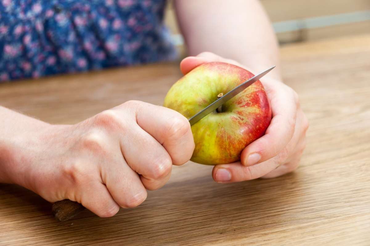Two hands hold a paring knife and an apple, ready to cut it.