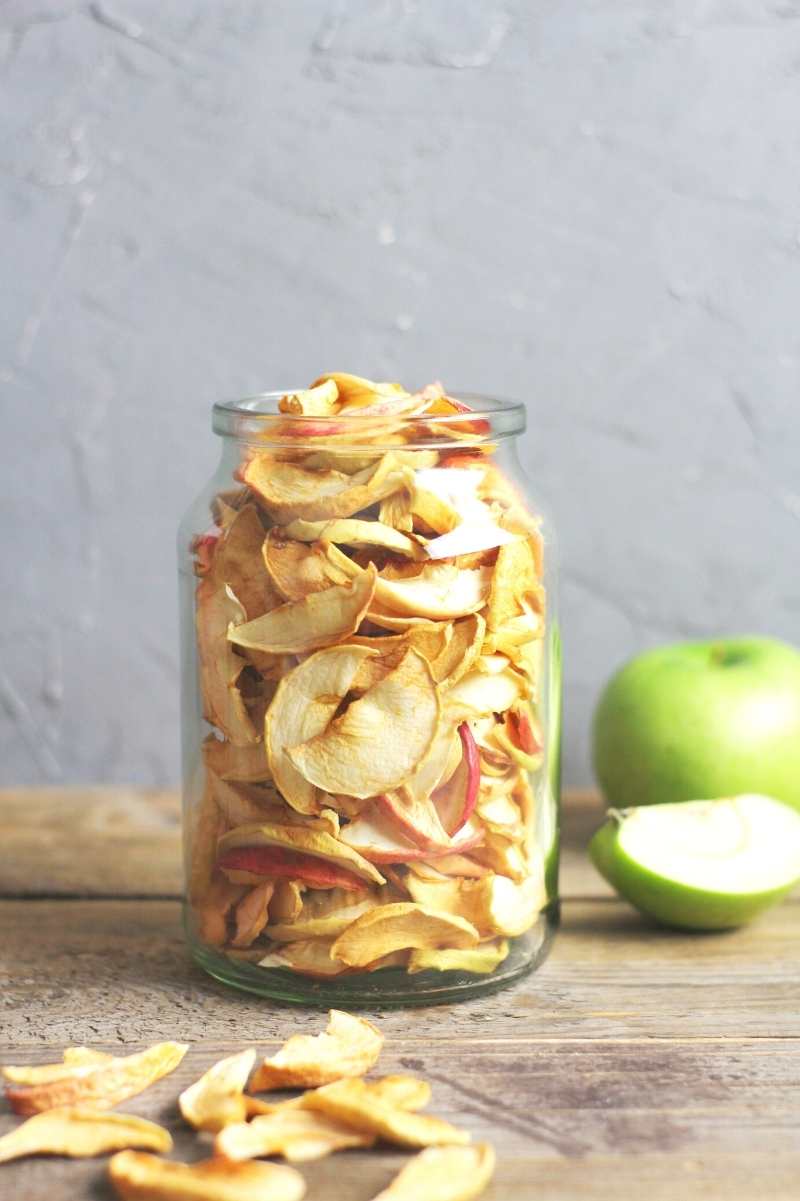 Apple chips in a glass jar on a wooden table.
