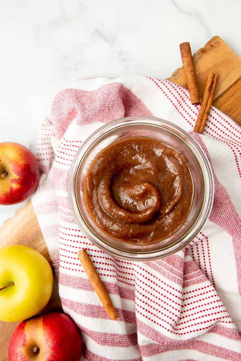 Instant Pot apple butter in a glass jar with whole cinnamon sticks and apples around it.