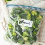 A full freezer bag labeled "Broccoli!" rests on a kitchen linen.
