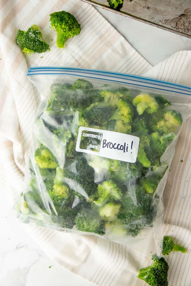 A full freezer bag labeled "Broccoli!" rests on a kitchen linen.