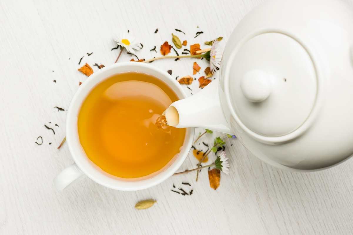 A white teapot pours tea into a white teacup.