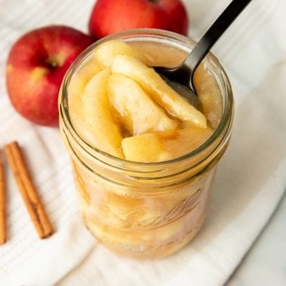 A spoon scoops apple pie filling from a Ball canning jar.