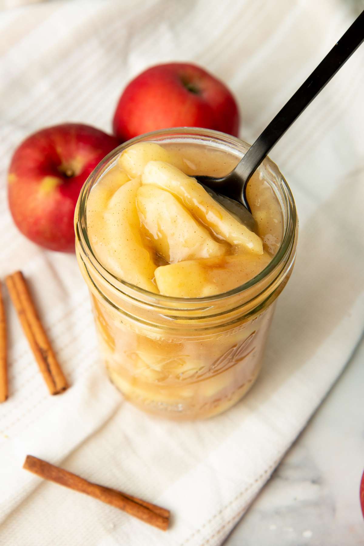 A spoon scoops apple pie filling from a Ball canning jar.