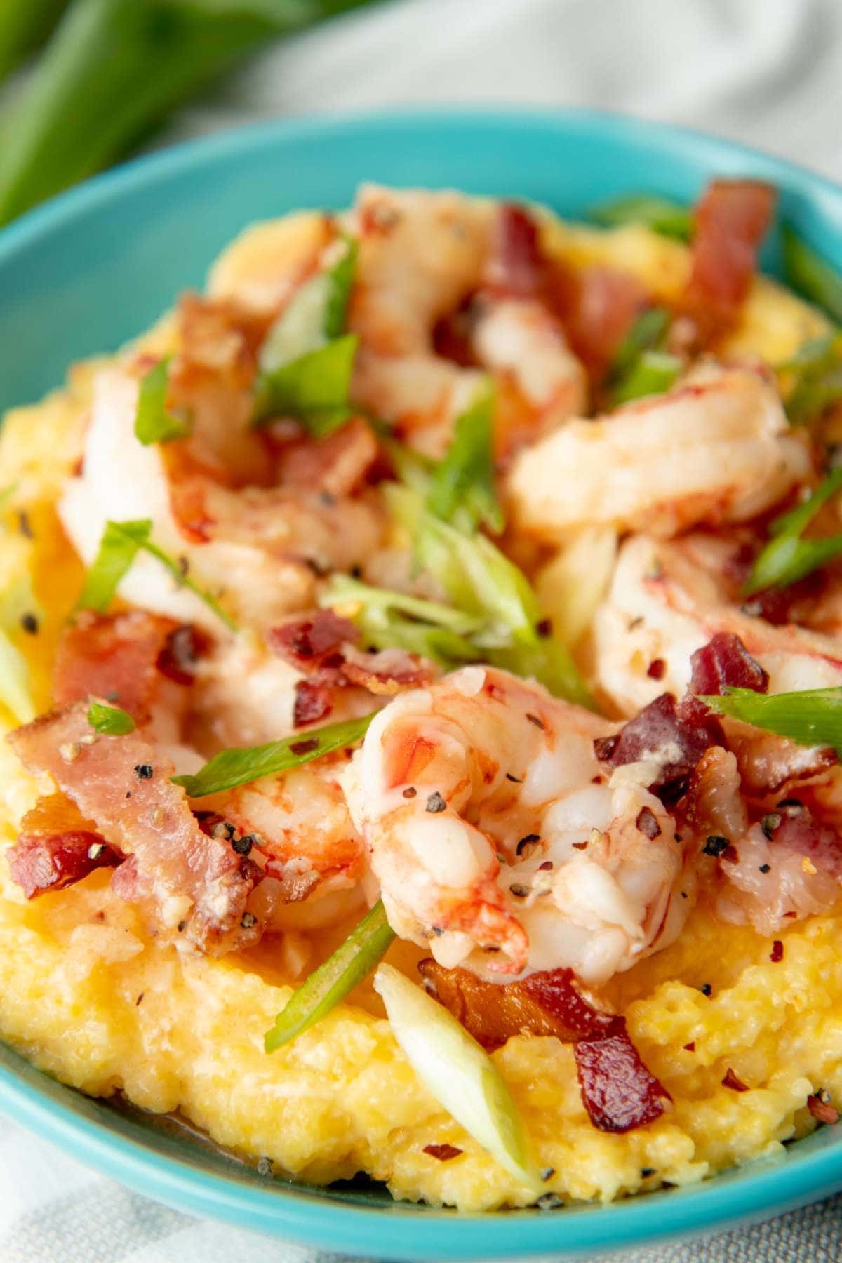 Close up of a teal bowl filled with grits topped with shrimp, bacon, and green onions.