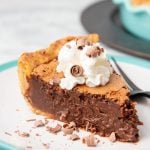 A slice of chocolate chess pie garnished with whipped cream and chocolate curls sits on a plate.