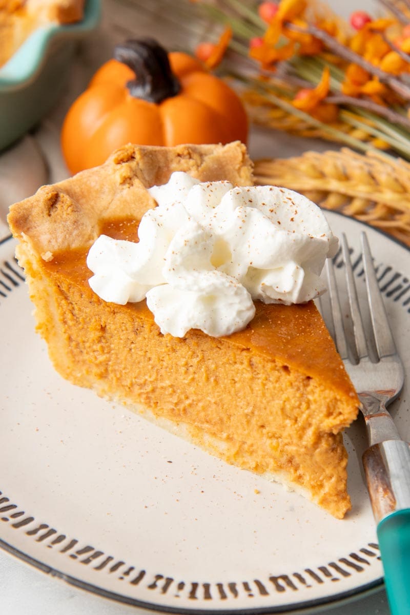 Close view of a creamy slice of pumpkin pie with whipped cream on top.