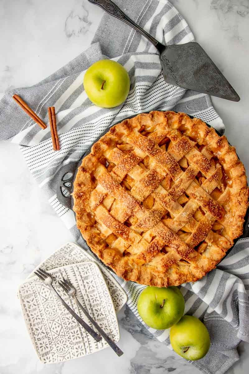 Finished pie overhead with whole apples, forks, and a pie server around it.