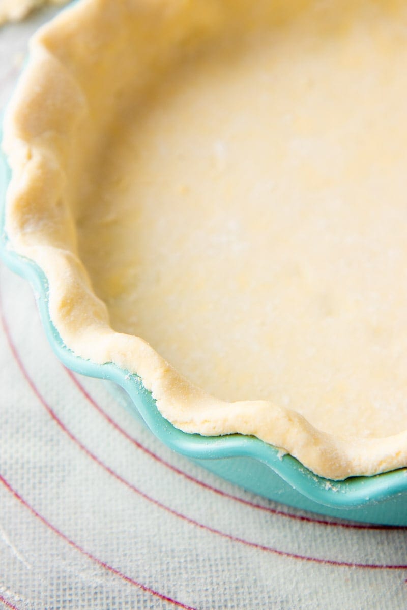 Close view of the fluted edge of an unbaked pie crust in a teal pie plate.