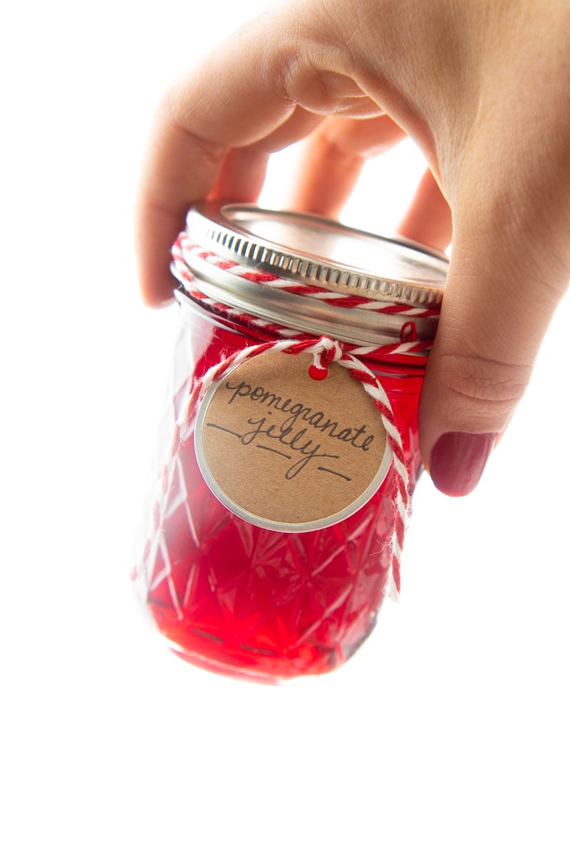 A hand holds up a small jar of perfectly clear jelly.