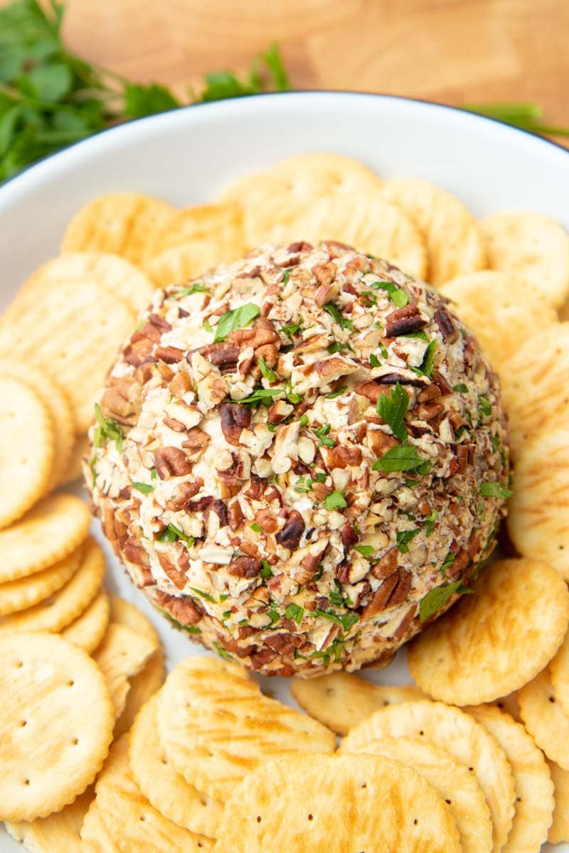 Classic cheese ball rests on a serving platter surrounded by buttery crackers.