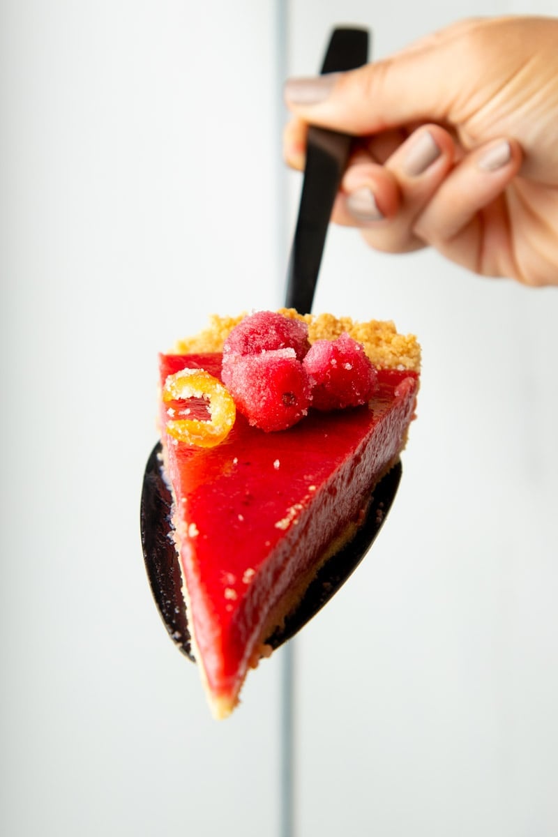 A hand holds up a pie serve with a garnished slice of cranberry curd tart on it.