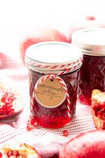 A gift tag tied with red and white string hangs from a jar of ruby red pomegranate jelly.