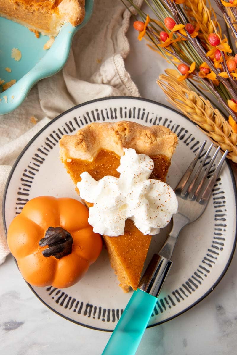 Overhead of a garnished slice of pumpkin pie on a plate with a fork.