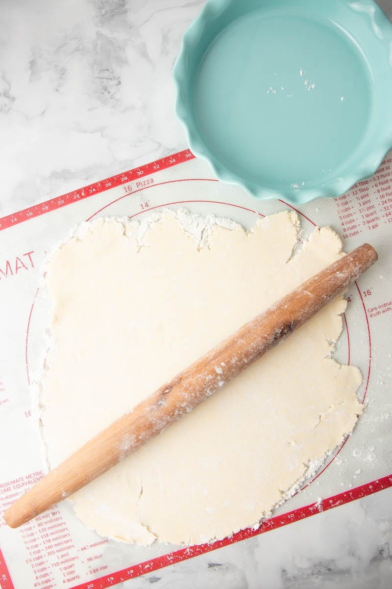 Overhead of gluten-free crust rolled out on silicone mat with a French-style rolling pin.