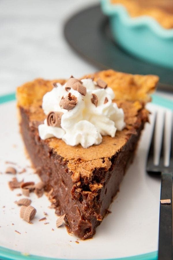 Front view of a slice of chocolate chess pie with whipped cream and chocolate curls on top.