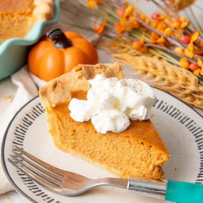 A single slice of pumpkin pie garnished with whipped cream sits on a plate with a teal-handled fork.