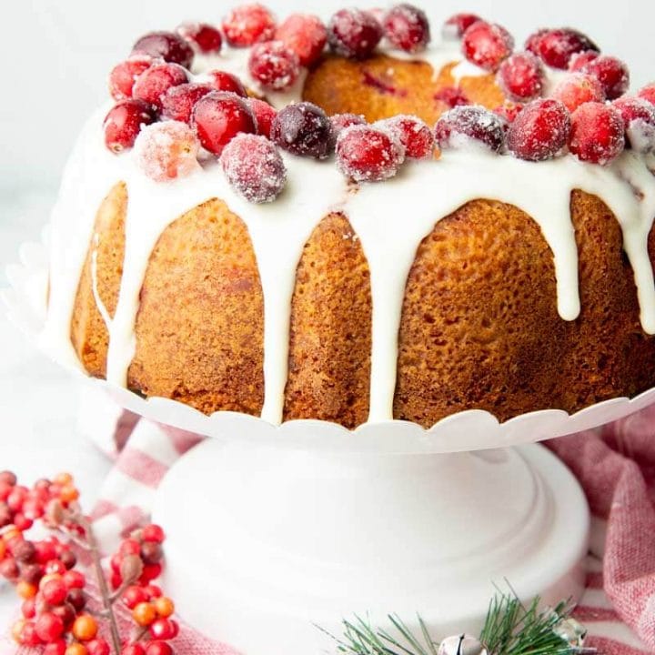 Sugared cranberries atop a thick white glaze that's dripping down the sides of the cranberry Christmas cake.