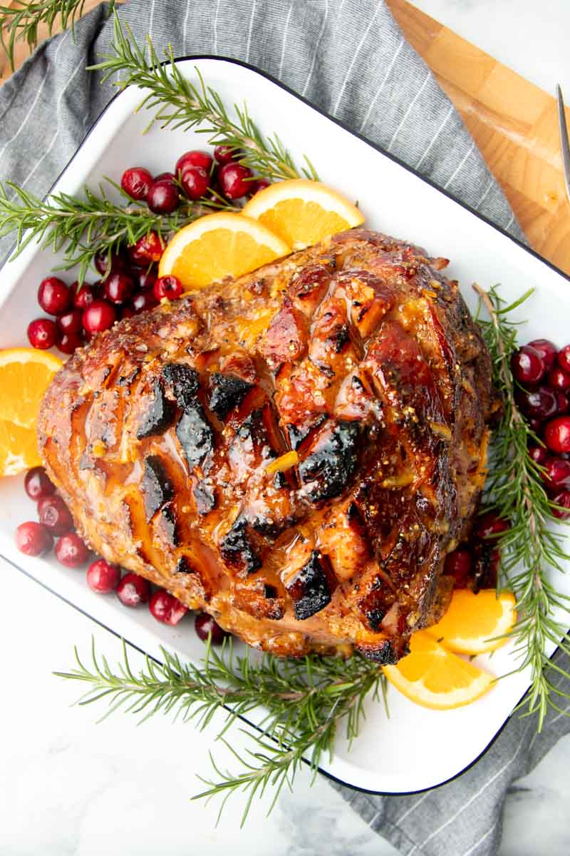Top view of bourbon glazed Christmas ham with fresh rosemary sprigs, orange slices, and cranberries.