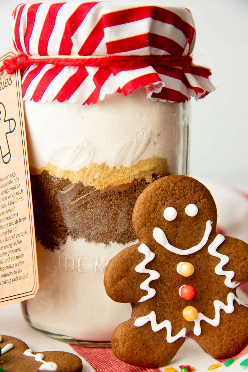 Close view of gingerbread cookie mix in a Ball quart jar with a gingerbread cookie standing up against it.