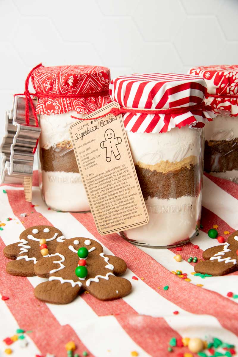 Three Ball wide mouth quart jars filled with gingerbread cookie mix and packaged for gifting with recipe tags and cookie cutters.