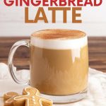 A gingerbread latte in a glass mug. Two gingerbread cookies sit next to the mug. A text overlay reads "Starbucks Copycat Gingerbread Latte."