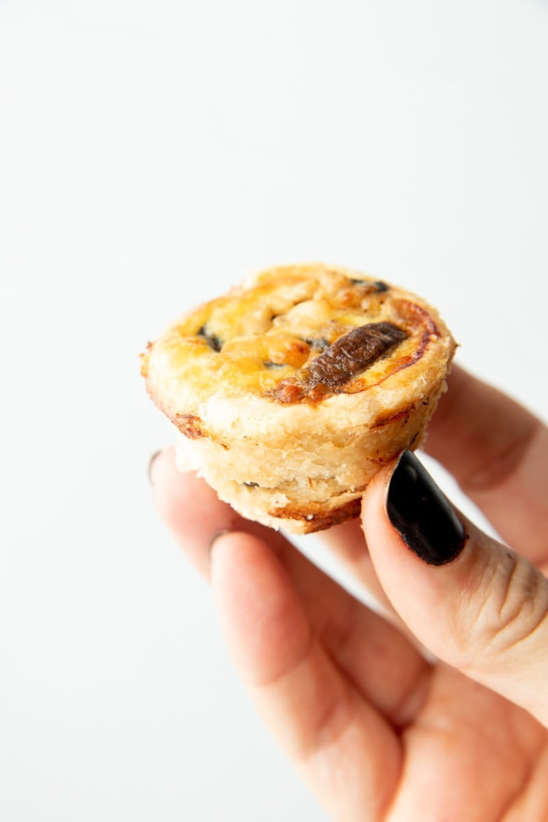A hand holds up a mini quiche appetizer.