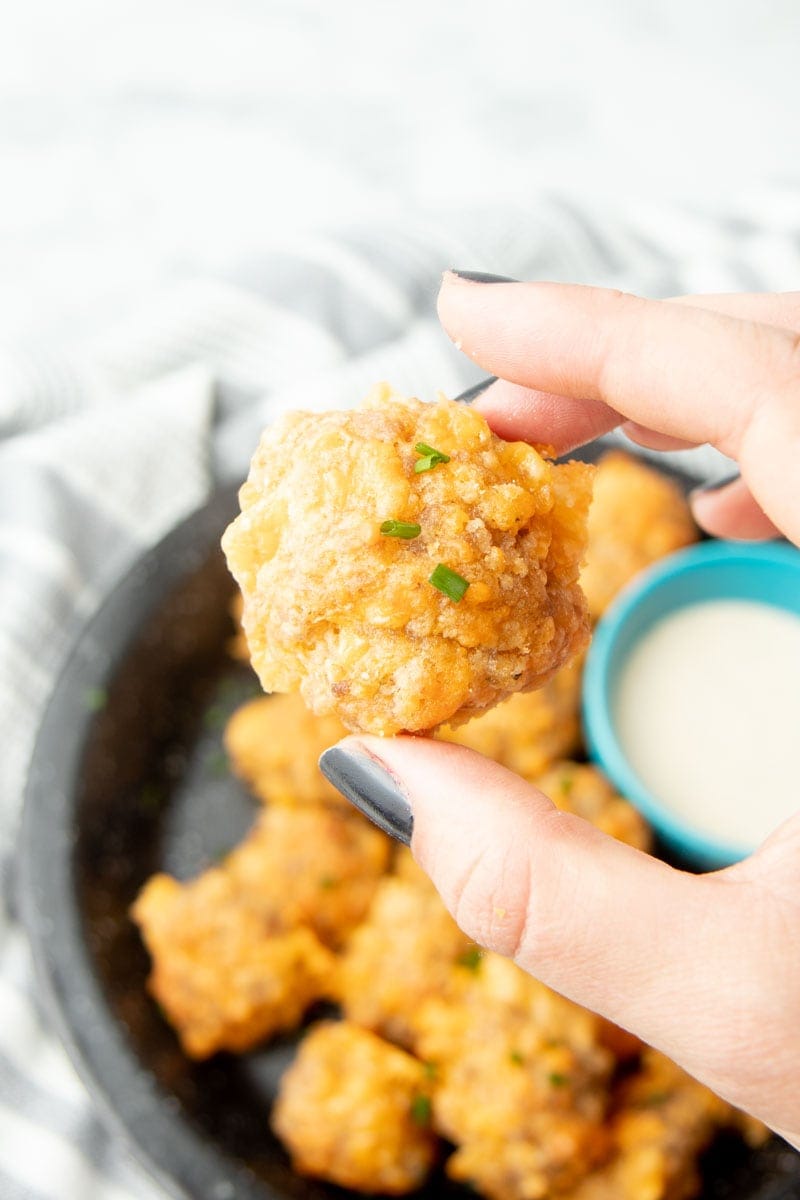 A hand holds a cheesy appetizer garnished with fresh snipped chives.