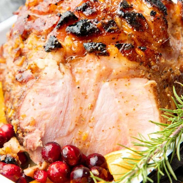 Sliced bourbon glazed ham in a roasting pan with fresh cranberries and orange slices.