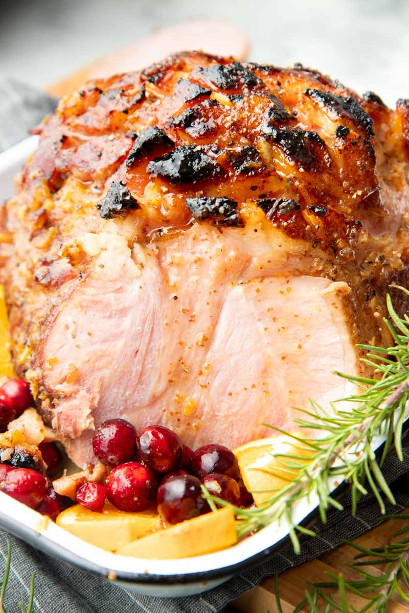 Sliced bourbon glazed ham in a roasting pan with fresh cranberries and orange slices.