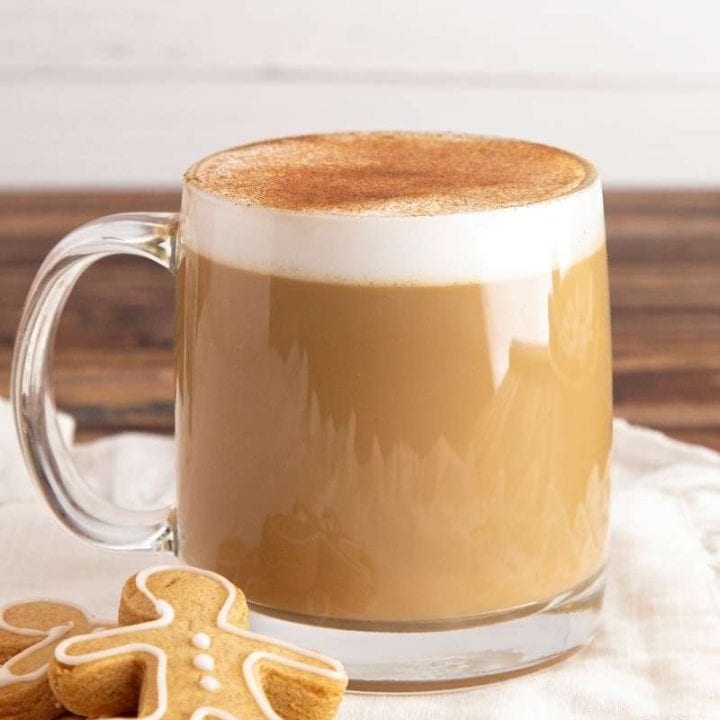 A gingerbread latte in a glass mug. Two gingerbread cookies sit next to the mug.