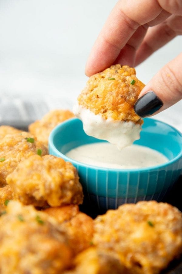 A hand holding a sausage ball dipped in ranch dressing.