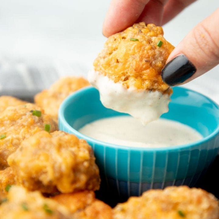 A hand holding a sausage ball dipped in ranch dressing.