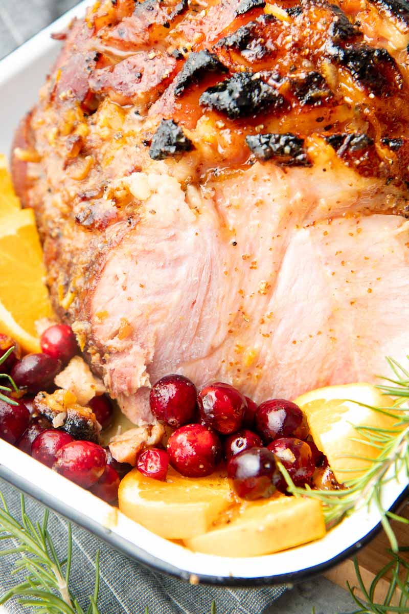 Sliced Christmas ham with bourbon glaze dripping down, nestled in fresh cranberries and orange slices.