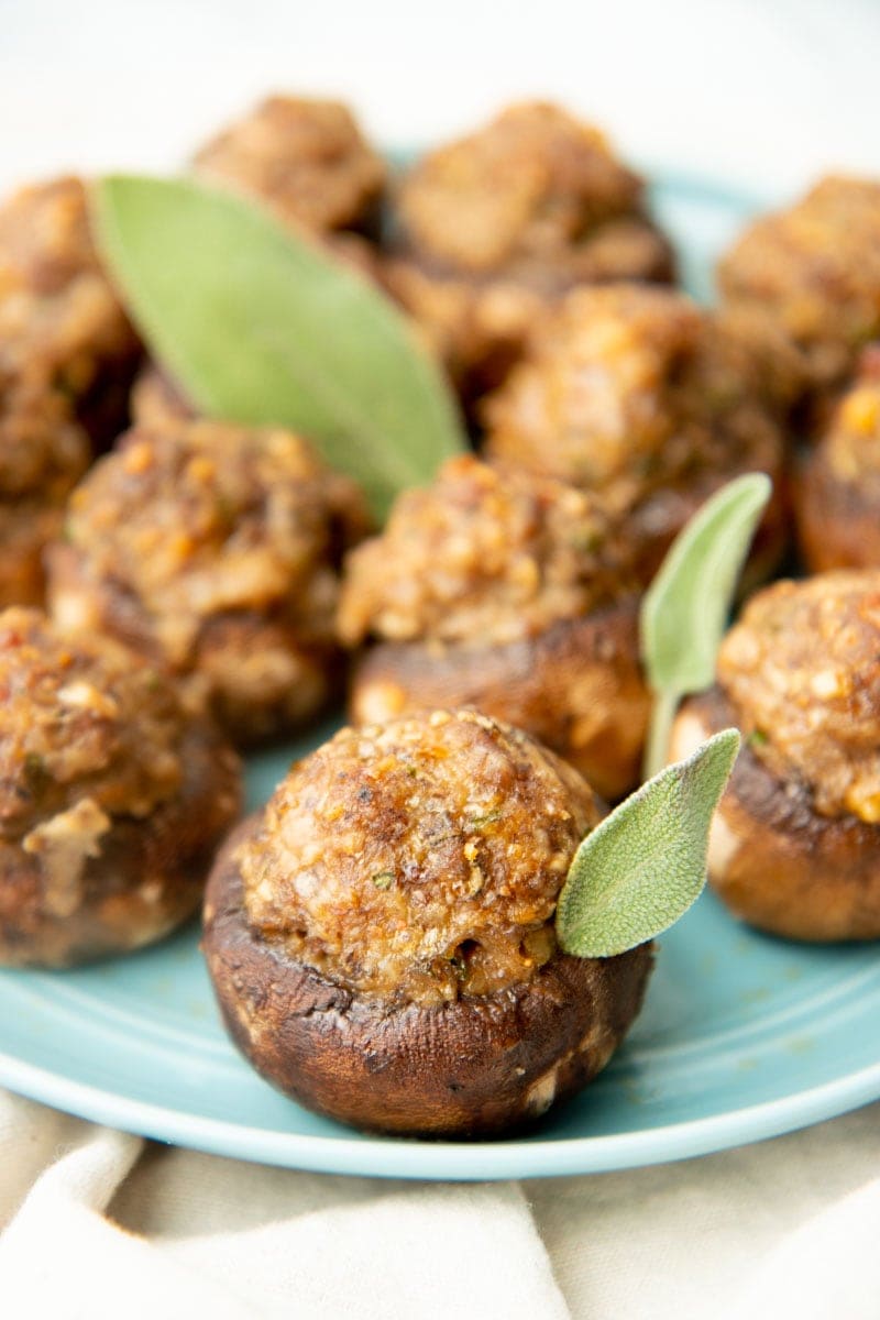 Sausage stuffed mushrooms on a plate garnished with sage.
