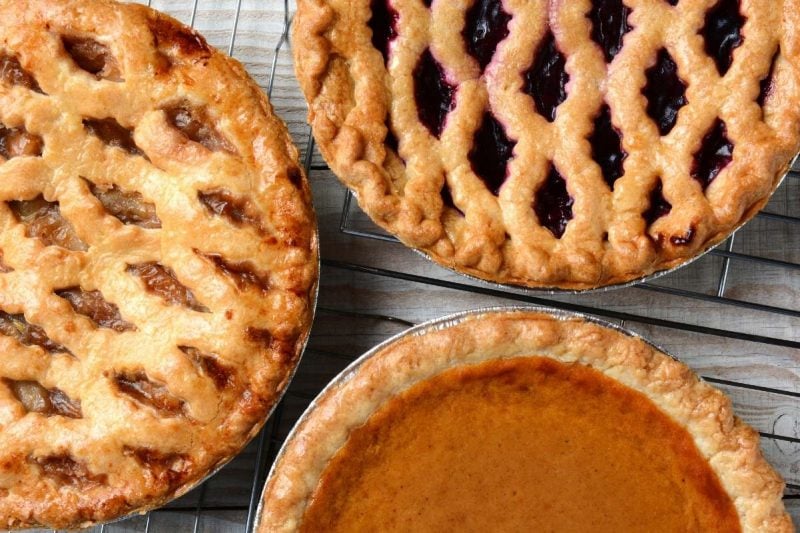 Three baked Thanksgiving pies sit together on wire cooling racks.