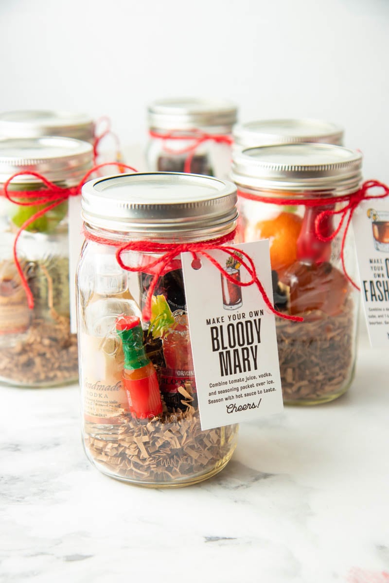 Six cocktail gifts in quart sized mason jars packaged for gifting with red ribbon and gift tags.