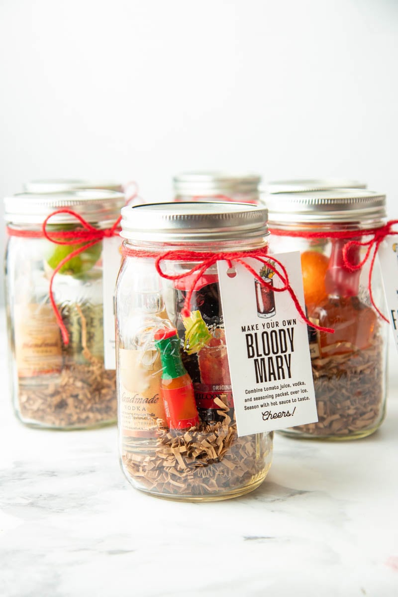 A bloody mary cocktail kits with a gift tag and red ribbon stands in front of 5 other cocktail gift kits.
