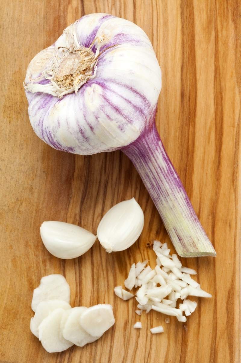 A head of garlic rests alongside sliced and minced garlic cloves.