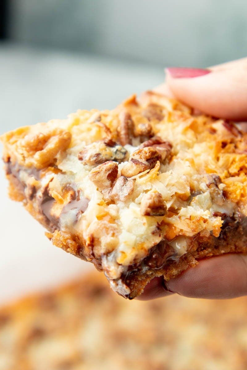 Close view of a gooey magic cookie bar held in a hand.