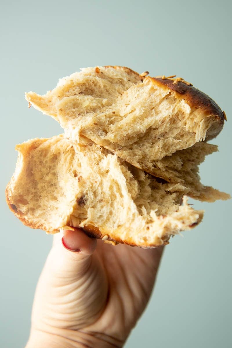 A hand holds up two torn pieces of finnish cardamom bread.