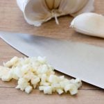 A small pile of minced garlic sits next to a large knife.