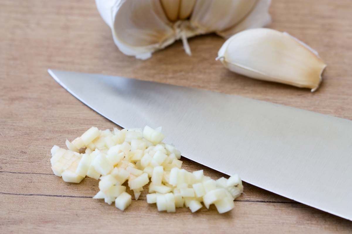 A small pile of minced garlic sits next to a large knife.