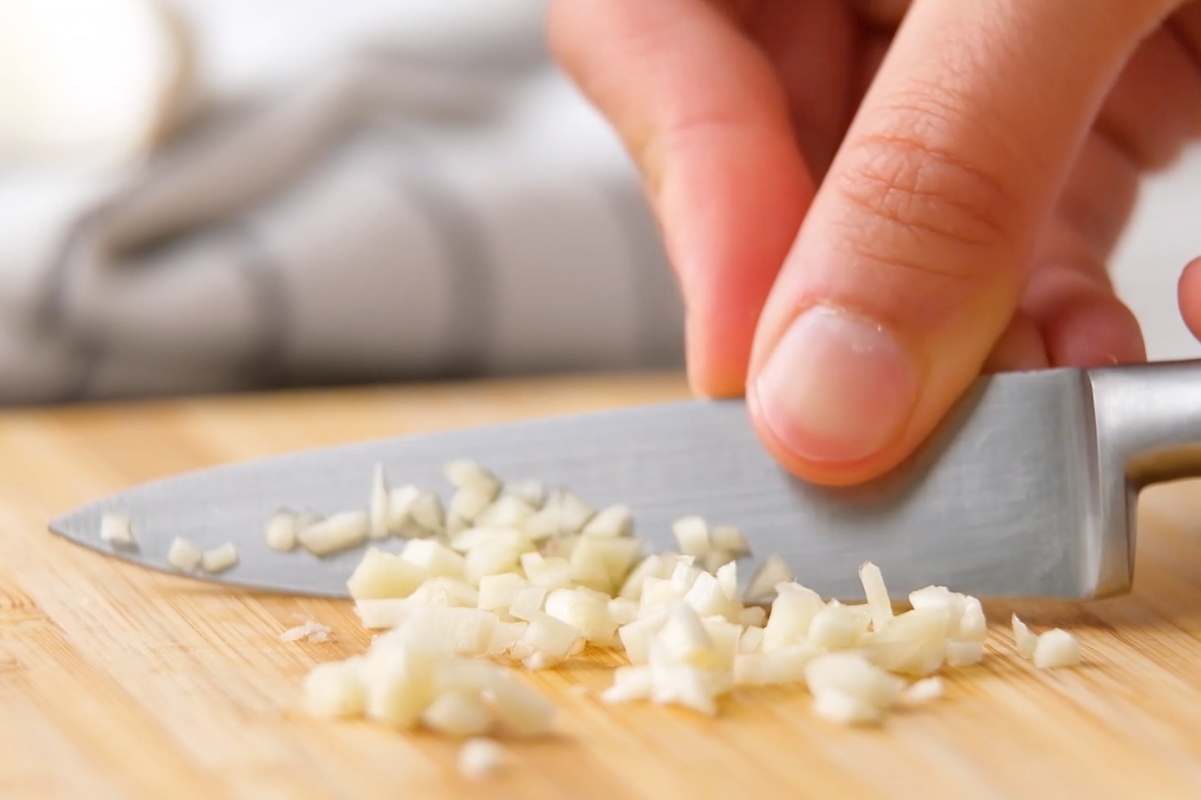 Tight view of a hand holding a knife that's mincing garlic.
