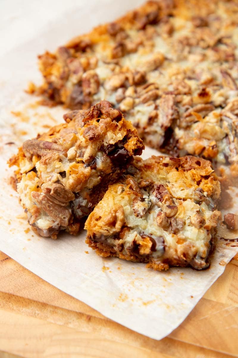 Two gooey seven layer bars stacked on parchment paper.