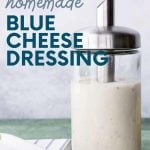 Close view of homemade blue cheese dressing in a glass bottle for pouring. A text overlay reads, " Easy. Healthy. Cheap. Homemade Blue Cheese Dressing."