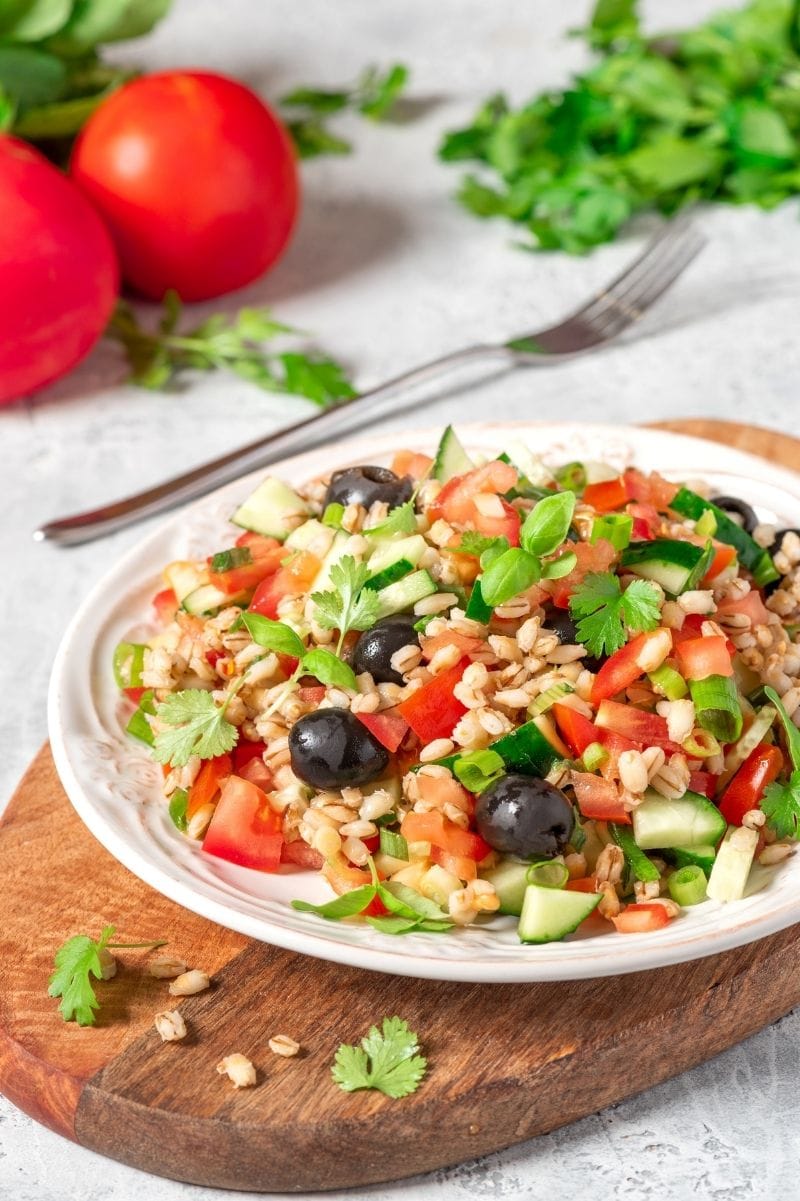 Colorful dish of cooked barley and fresh vegetables such as tomatoes and cucumbers on a plate.