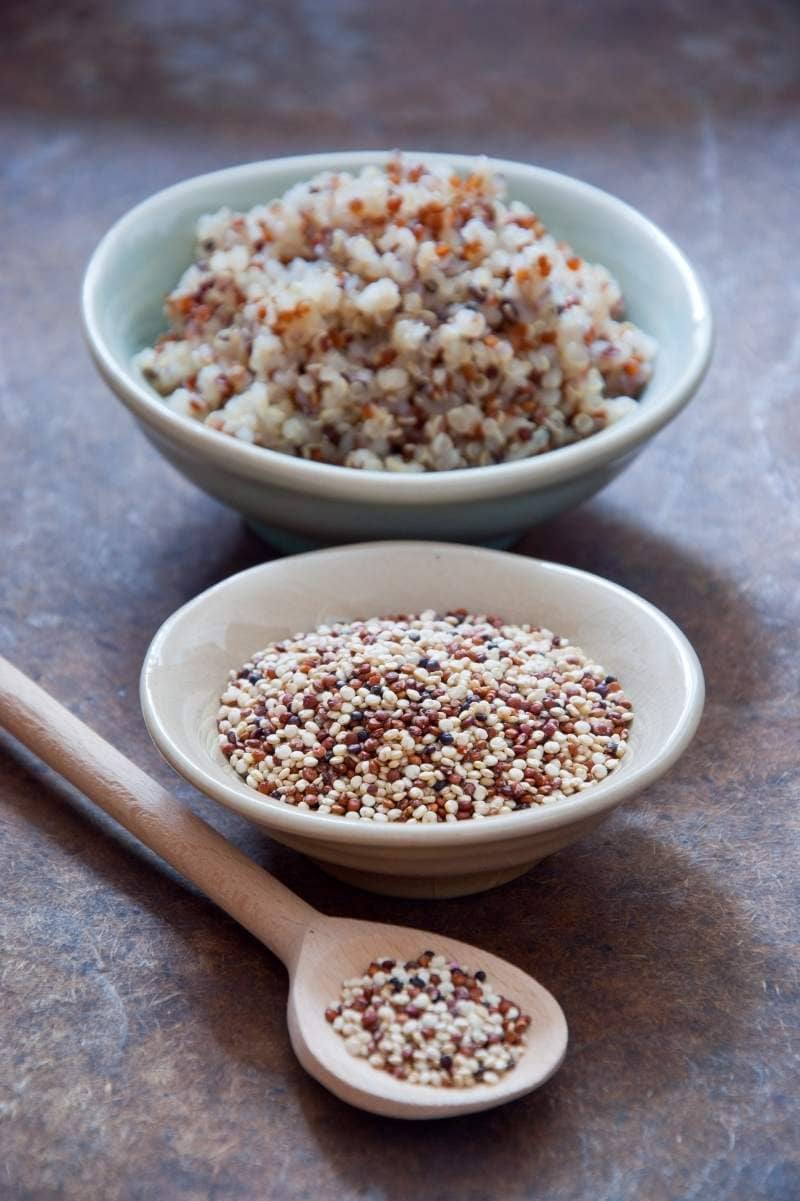 Two bowls and a wooden spoon lined up top to bottom and filled with quinoa.