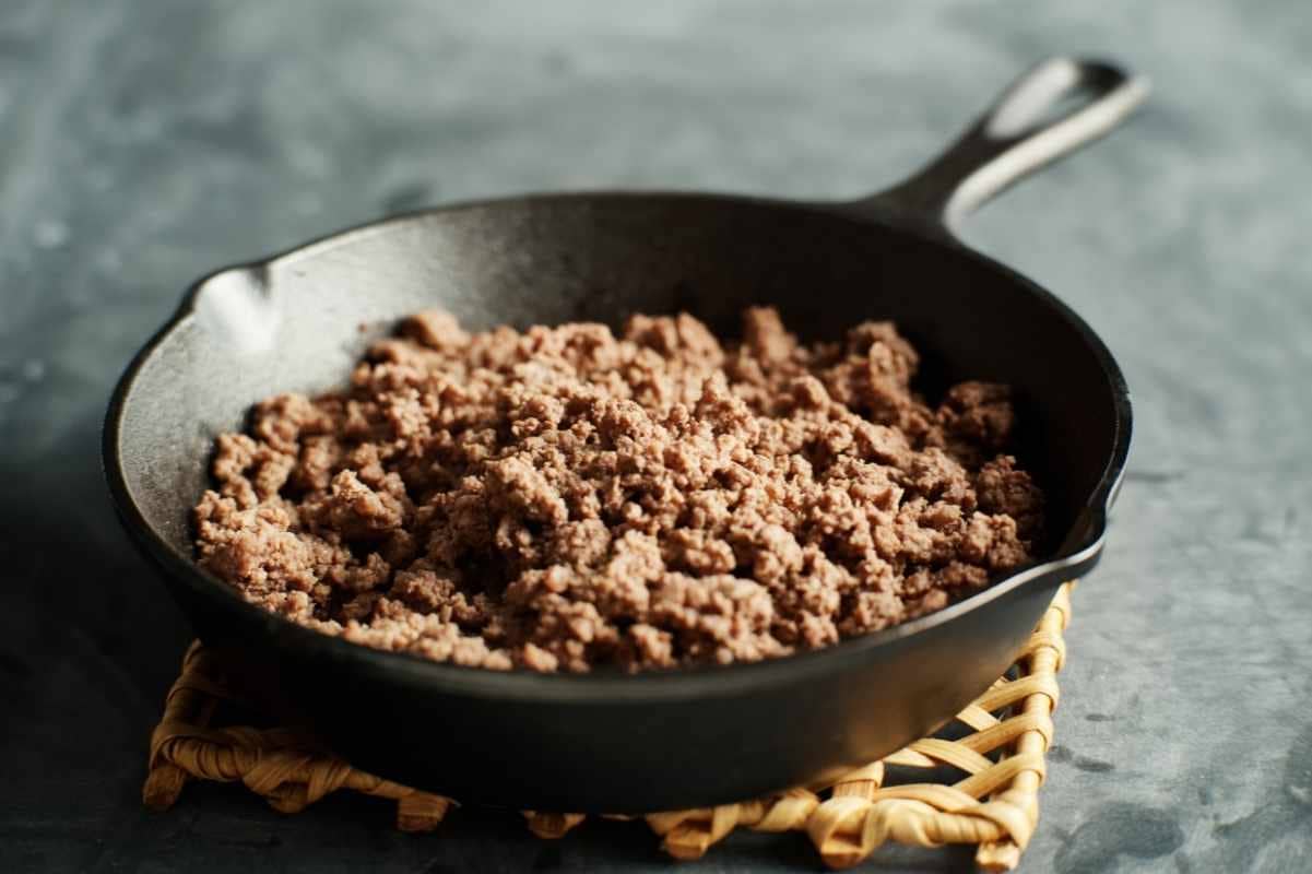 Close view of browned beef in a cast iron skillet on a trivet.