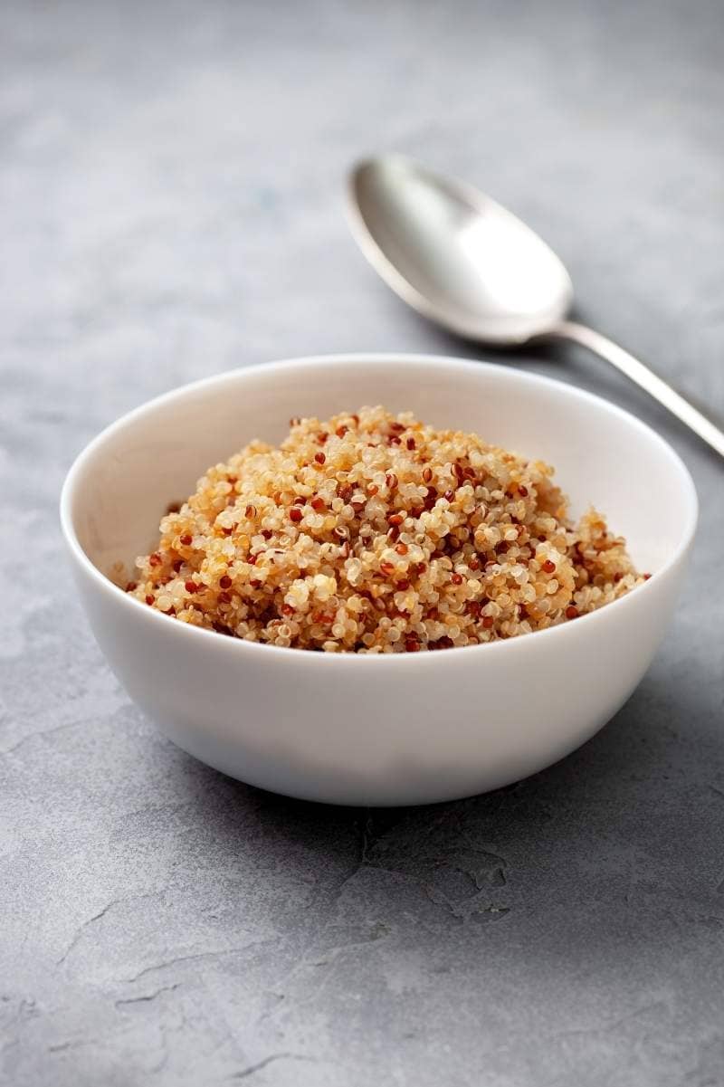 Perfectly cooked quinoa in a white bowl with a spoon in the background.